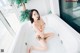 A woman sitting in a bathtub with a plant in the background.