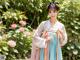 A woman in a blue and pink hanbok standing in a garden.