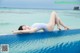 A woman in a blue swimsuit laying on the edge of a swimming pool.