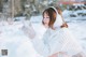 A woman in a white sweater and white gloves in the snow.