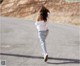 A woman in a white shirt and jeans running down a road.