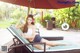 A woman sitting on a lounge chair under an umbrella.